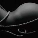Black and white high-contrast image of a body tied with rope, emphasizing curves.
