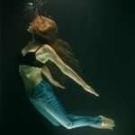 A captivating underwater photo of a woman in jeans and a bra, floating gracefully.