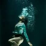 Dramatic photo of a woman diving underwater in stylish attire.