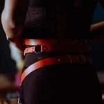 Back view of crop anonymous female in black panties corset and leather belt standing in dressing room and looking in mirror